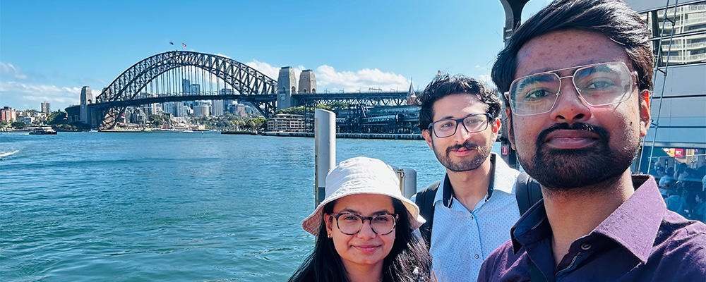 Ketan and two friends enjoy the sun at Sydney harbour with the Sydney Harbour Bridge behind them.