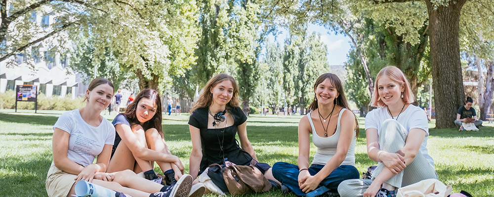 Five young women sitting on the lawns of University Ave enjoying the sunshine.