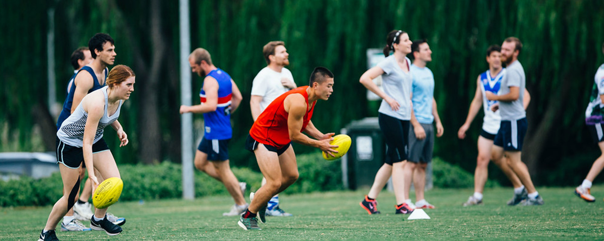 A mixed footy team practising on a grassy oval.