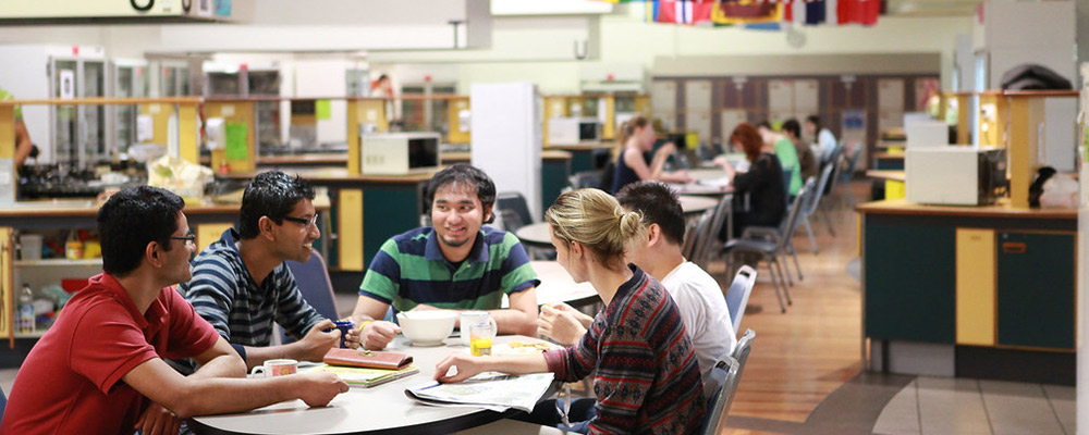 A group of students eat and chat at a table in a self-catered residence.