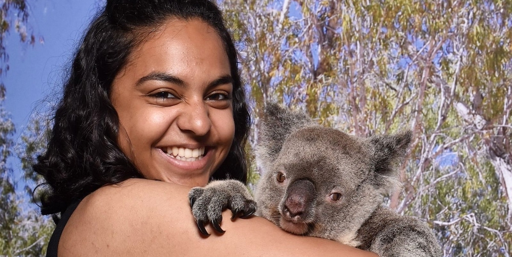  Priya stands and hugs a koala, which is holding onto her.