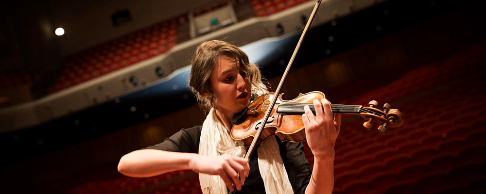 A young woman plays violin on stage at Llewellyn Hall.