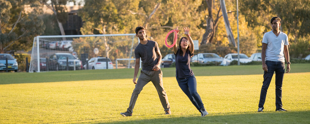 A group of students play frisbee on an oval at ANU.