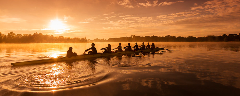 A group of ANU students row across Lake Burley Griffin at sunrise.