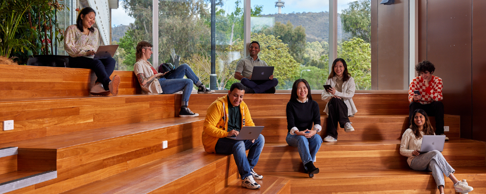 ANU students sit on large wooden benches overlooking Black Mountain.