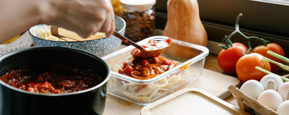 A person prepping their fresh food into a glass storage container.