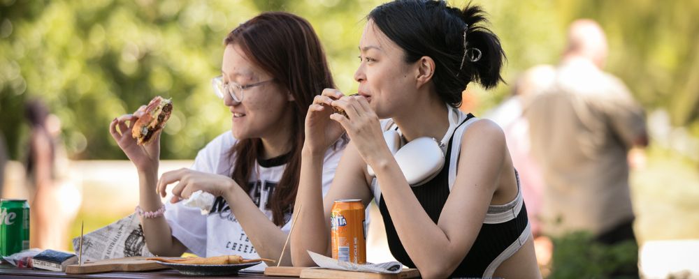 Two ANU students enjoying their food together on an outside table at the ANU Kambri precinct.