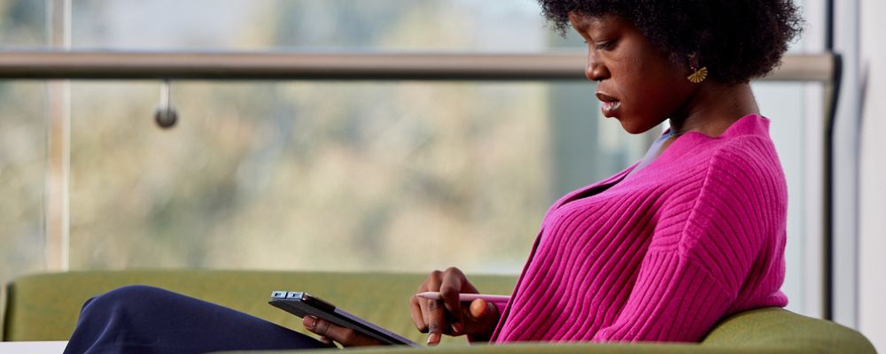 Female student sitting on chair inside an ANU study space using an app on her smart device.