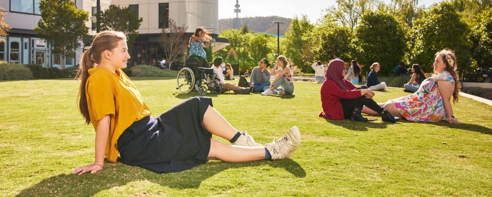 ANU students sit in the sun on Kambri Lawns.