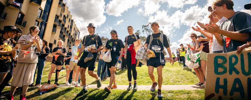 ANU students cross the finish line of the Inward Bound inter-residential race in front of other residents on campus at ANU.