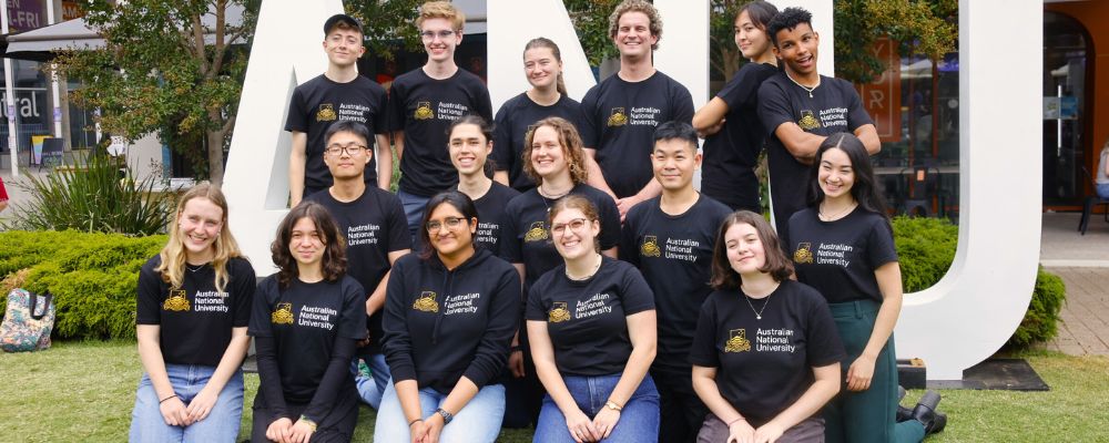 ANU student ambassadors pose together in front of an ANU sign at ANU Open Day.
