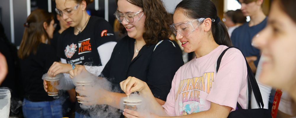 Female attendees of ANU Open Day do a science experiment at an expo stall hosted by one of the academic colleges. 