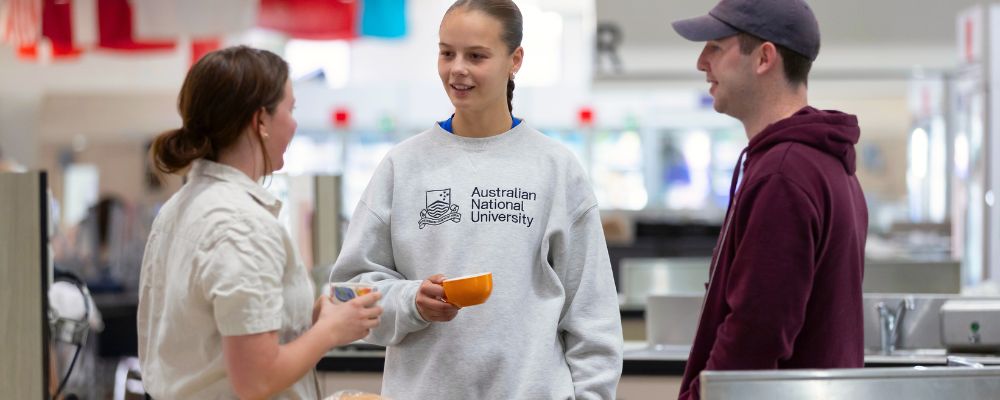 Three students chatting in a communal kitchen within a student residence at ANU