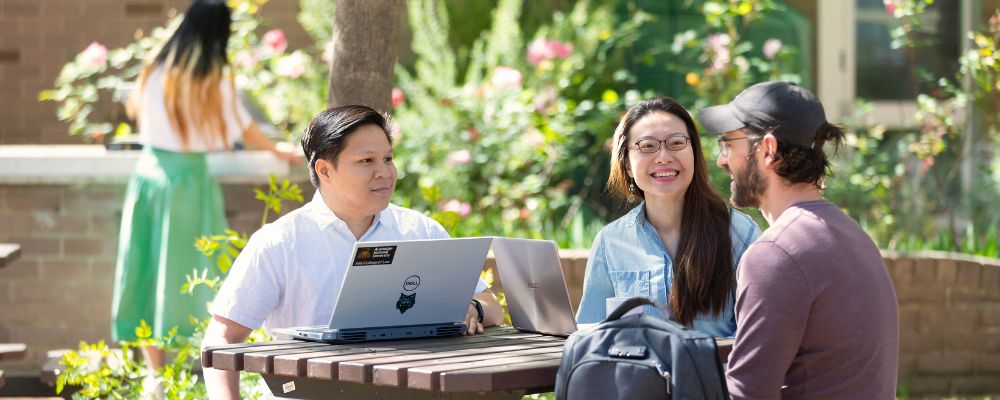 Three ANU students sit outside in an ANU student accommodation courtyard on campus.