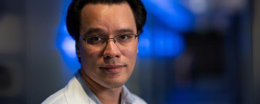 ANU researcher Simon Jiang looks into the camera with a blue blurry background out of focus.
