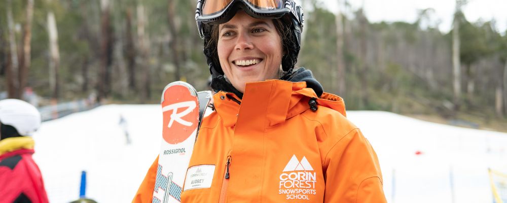 A woman wearing snow headgear and holding ski equipment on the slopes at Corin Forest