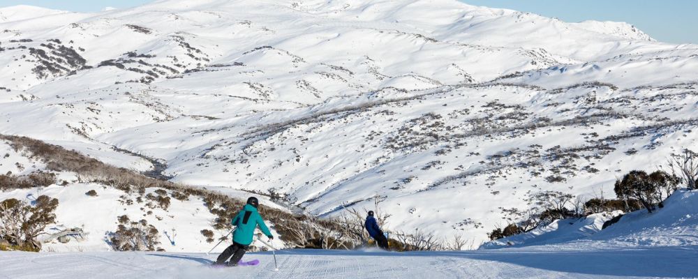 Two individuals ski and snowboard down a slope at the Perisher Ski Resort.