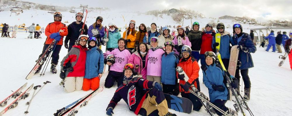 The ANU Snowsports social sports club standing together on the snow slopes posing for a photo.