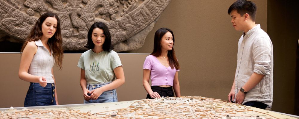 Four ANU students standing together over a tactical diorama in the School of Archaeology and Anthropology.