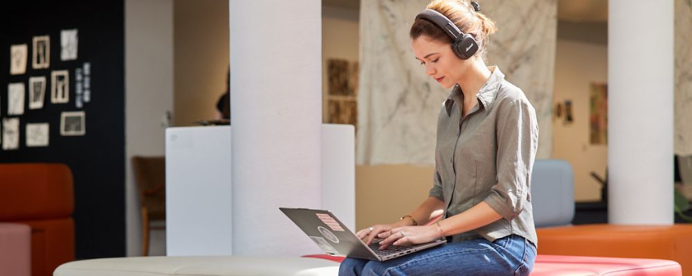 A student on a laptop in an ANU study space working with headphones on.