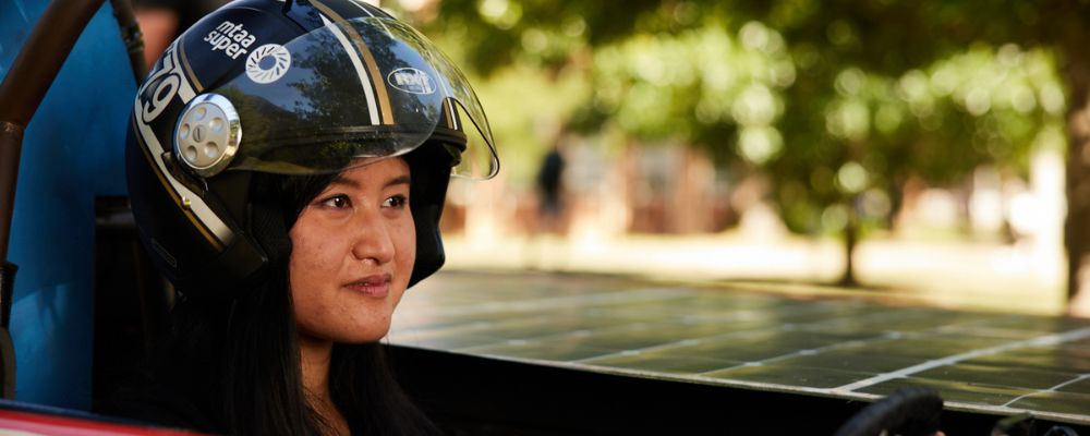 A female ANU student wearing a helmet and sitting in the ANU Solar Racing team car.