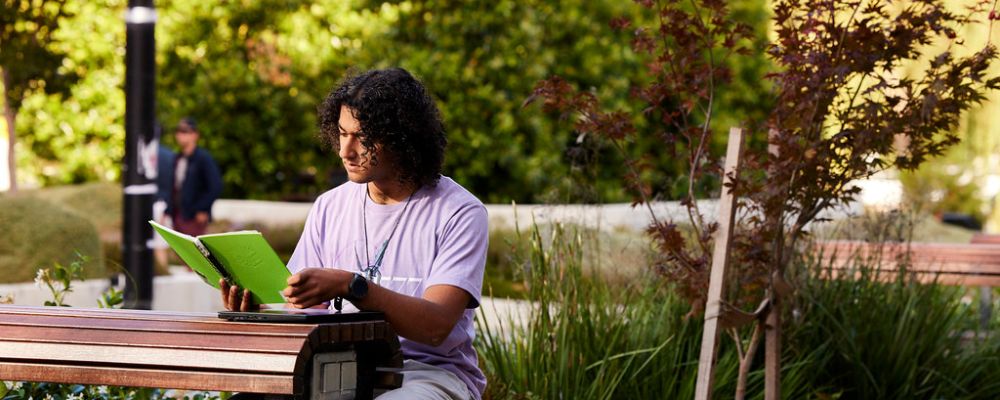 A male ANU student studies outside on an outside table on the Australian National University campus.
