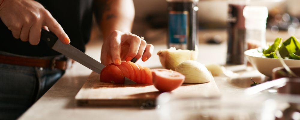 A woman chopping tomatoes and onion on a wooden chopping board in a home kitchen.
