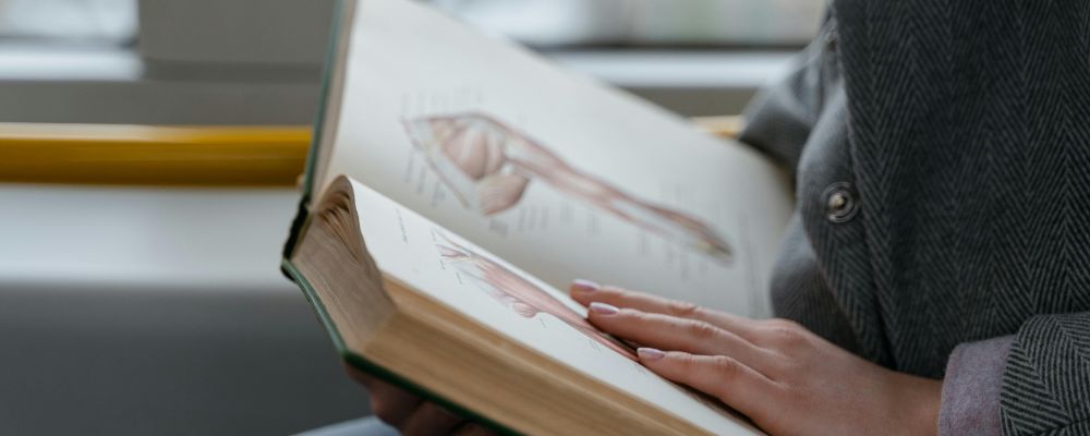A person in a grey coat reads an anatomy textbook.