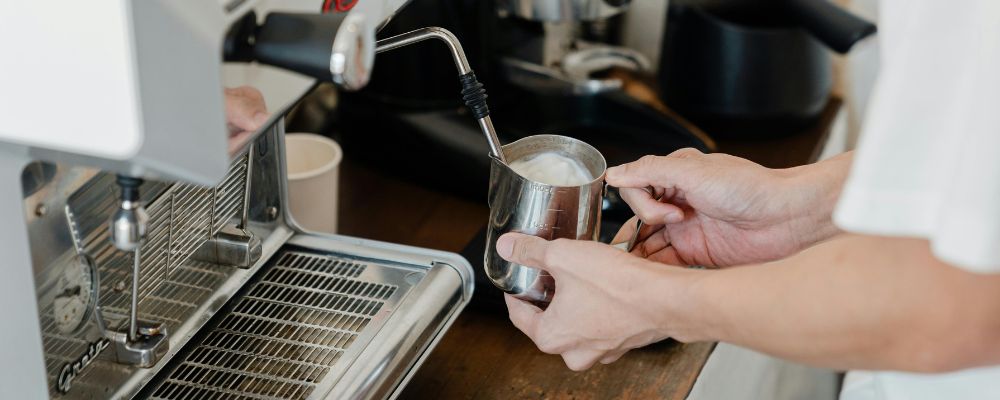 A young barista frothing milk behind the counter at a café.
