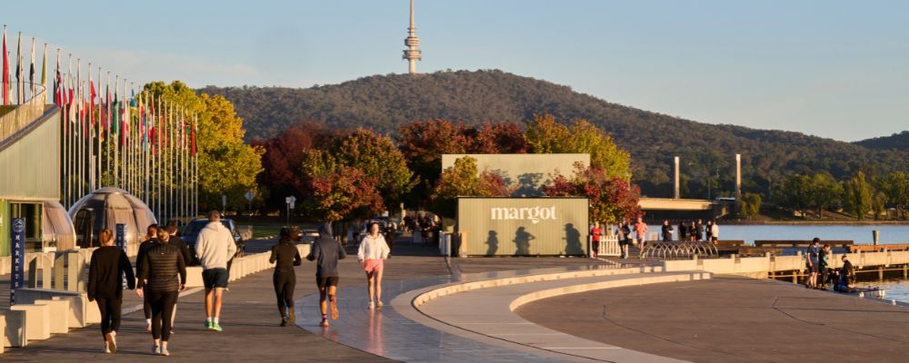 Sunrise scene at Reconciliation Place beside Lake Burley Griffin with a view to Black Mountain and Telstra Tower in the background. Locals and tourists are pictured exercising and catching up amongst the autumn leaves.