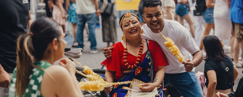 The exterior of the Multicultural Festival in Canberra, with people in traditional attire smiling and holding food.