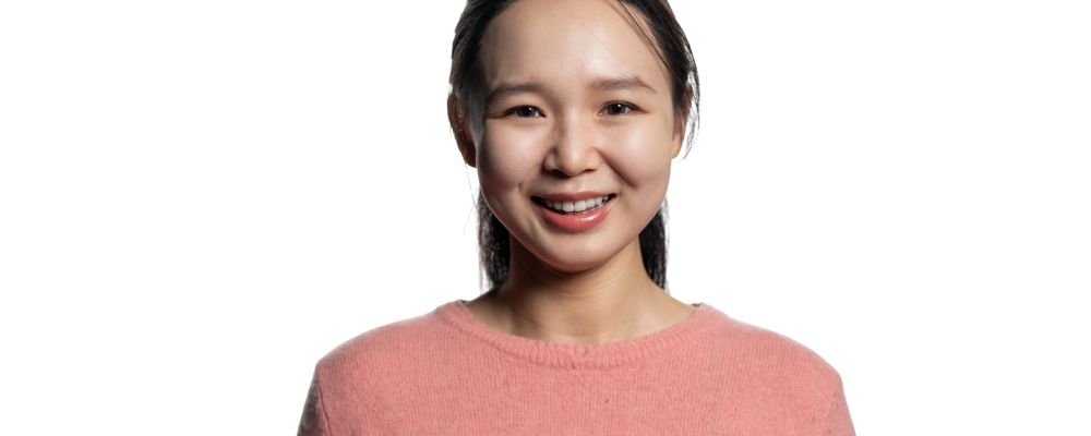 Yixi smiles at the camera wearing a pink cardigan in a photoshoot at the Australian National University