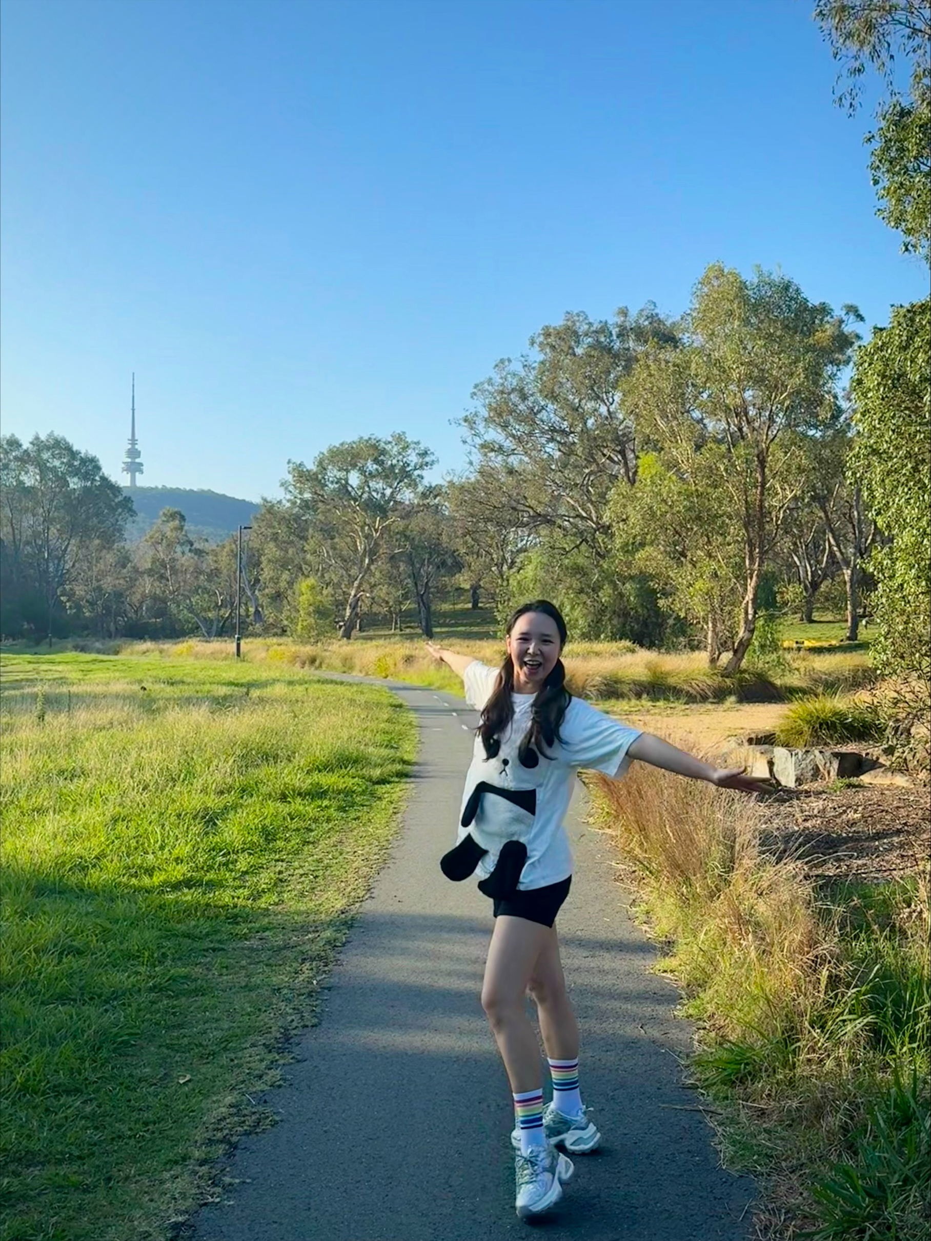 Yixi stands on a bike trail and poses for the camera on a sunny day in Canberra with Black Mountain Tower behind her.