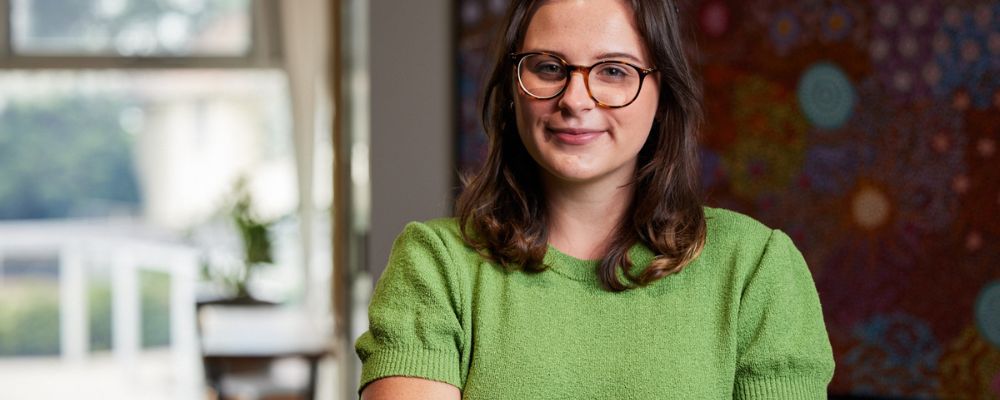 An ANU postgraduate student looks into the camera with arms folded and a smile.