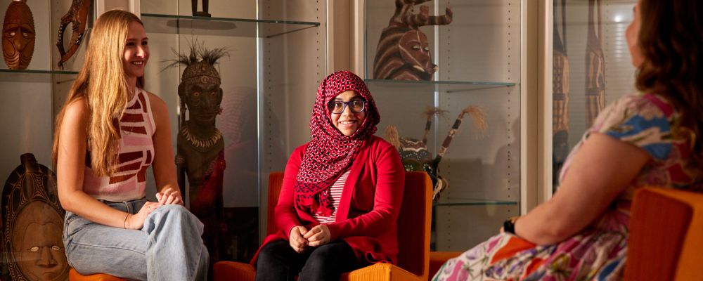 Three ANU students sit on communal seating together in discussion.