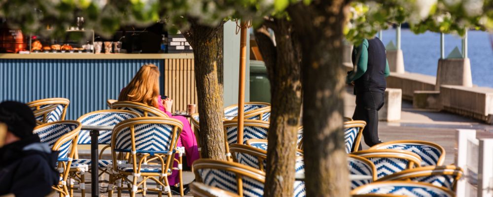 A woman sits outside Margot Wine & Espresso bar on a wicker seat, outdoor waterfront café in Canberra.