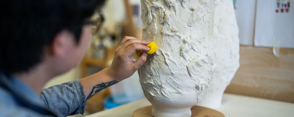 Nathan Nhan sponges a clay vessel, moistening it before it is to be fired in the kiln.