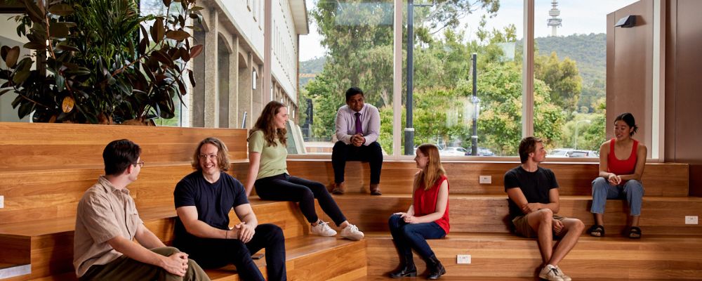ANU students sit on tiered seating together in a class, discussing learning topics.