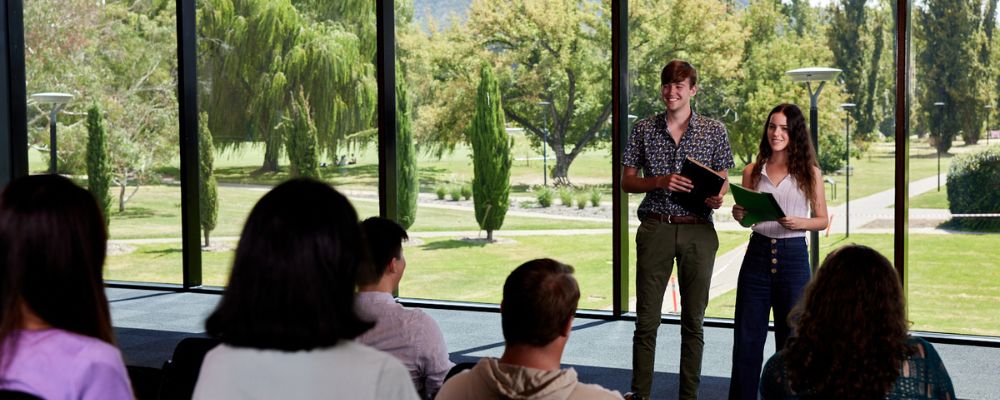 Two ANU students stand in front of their class at ANU, presenting research or their assignment.