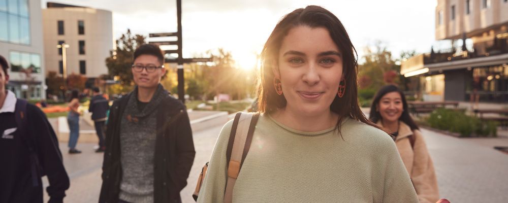 ANU students walk down University Avenue at sunset together, chatting and laughing.