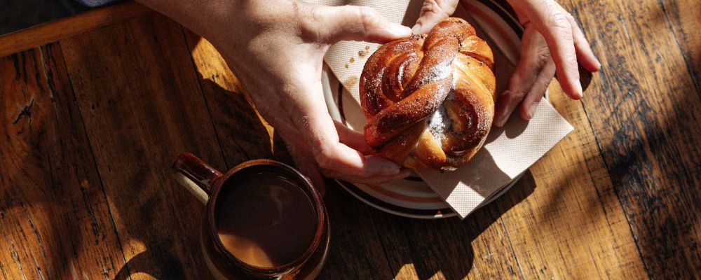 A cinnamon bun sits on a wooden table at Under Bakery with the sun shining across the top.