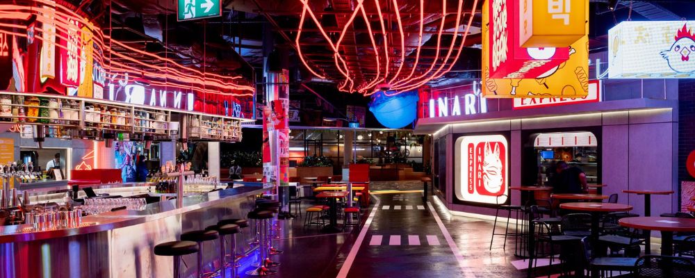 The interior view of Tiger Lane at night with neon lights and hawker style food vendors ready to serve customers.