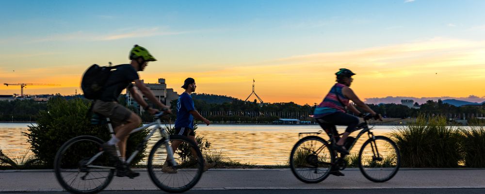 Three cyclists ride along Lake Burley Griffin at sunrise in Canberra.