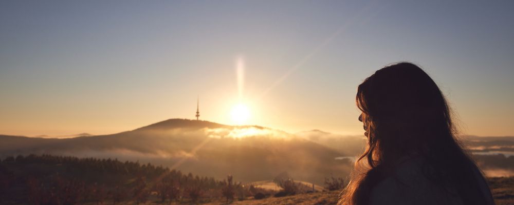 A female ANU student looks out over Canberra at sunrise, with Black Mountain Tower visible in the distance.
