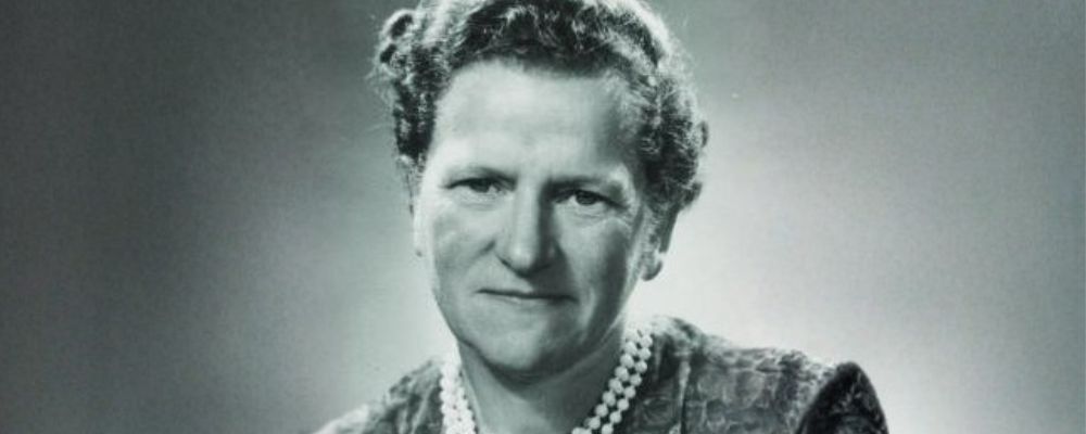 Hanna Neumann poses for a black and white portrait, wearing a pearl necklace and looking directly at the camera.