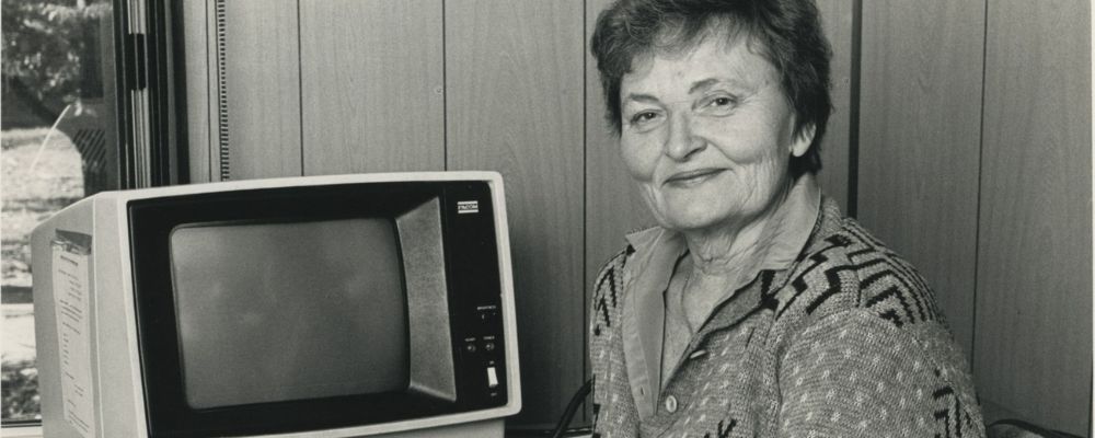 Skaidrite Darius sits beside an early computer terminal in a black and white portrait.