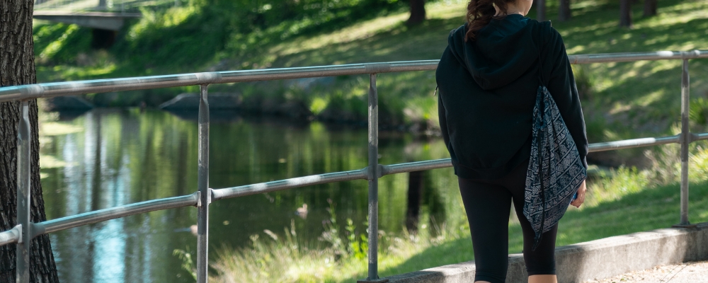 A female ANU student walks outside on campus with Sullivans Creek in the distance.